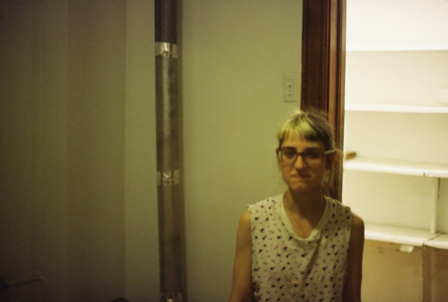 In this nearly identical shot, Lauren’s expression changes as she smiles warmly, her eyes open and engaging with the camera. The subtle glow of the lighting highlights her features and the same background elements—the pantry, pipe, and doorframe—remain visible, keeping the focus on her energy.