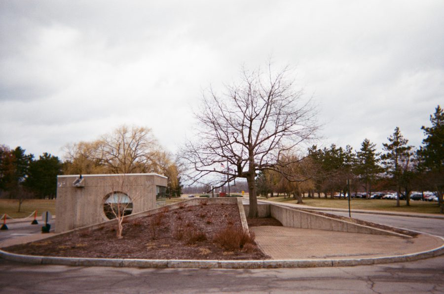 A concrete structure on the RIT campus with a circular window, a sloped walkway, and minimal landscaping. Bare trees and overcast skies add to the stark appearance of the scene.