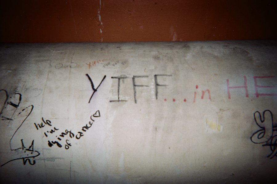 A close-up of graffiti on a pipe in the RIT tunnels. The words "YIFF… in HELL" are scrawled across the surface, surrounded by doodles, including a small drawing and a caption reading, "Help I'm dying of cancer."