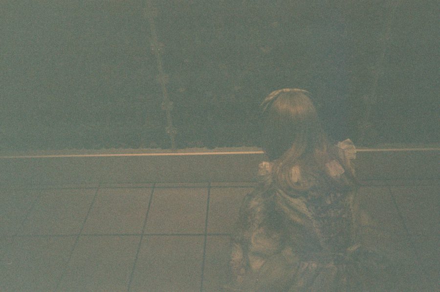 Lauren crouching in front of a large display of antique glass vials and jars. The dim lighting emphasizes the rows upon rows of vintage containers arranged meticulously in a museum-like setting.