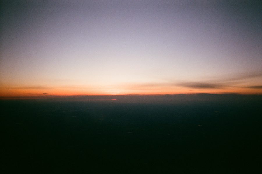 Another view of the sunset from the plane, with soft orange and red hues near the horizon fading into dark blue sky above. The faint curvature of the Earth is visible in the distance.
