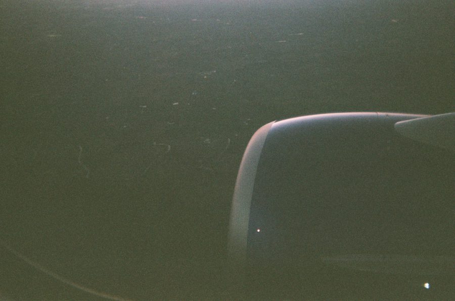 A plane engine captured mid-flight, with a faint view of the land far below, shrouded in early evening shadows.
