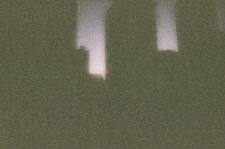 A blurry photo taken in Chicago, capturing abstract silhouettes of large buildings against a dimly lit sky. The light seems to seep through the gaps, creating a faint gradient effect. The image is grainy and unclear, evoking an atmospheric, almost ghostly impression of the city.
