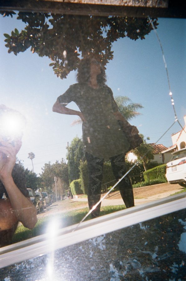 Marina reflected in a street mirror, with a secondary reflection of me crouching in the corner holding the disposable camera. The flash from the camera creates a bright spot in the otherwise detailed view of suburban West Hollywood, with tree-lined streets, a white car, and vibrant greenery.